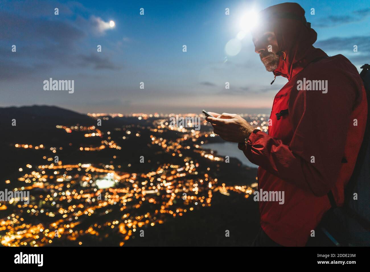 Uomo maturo che utilizza smartphone con città illuminata contro il cielo di notte Foto Stock