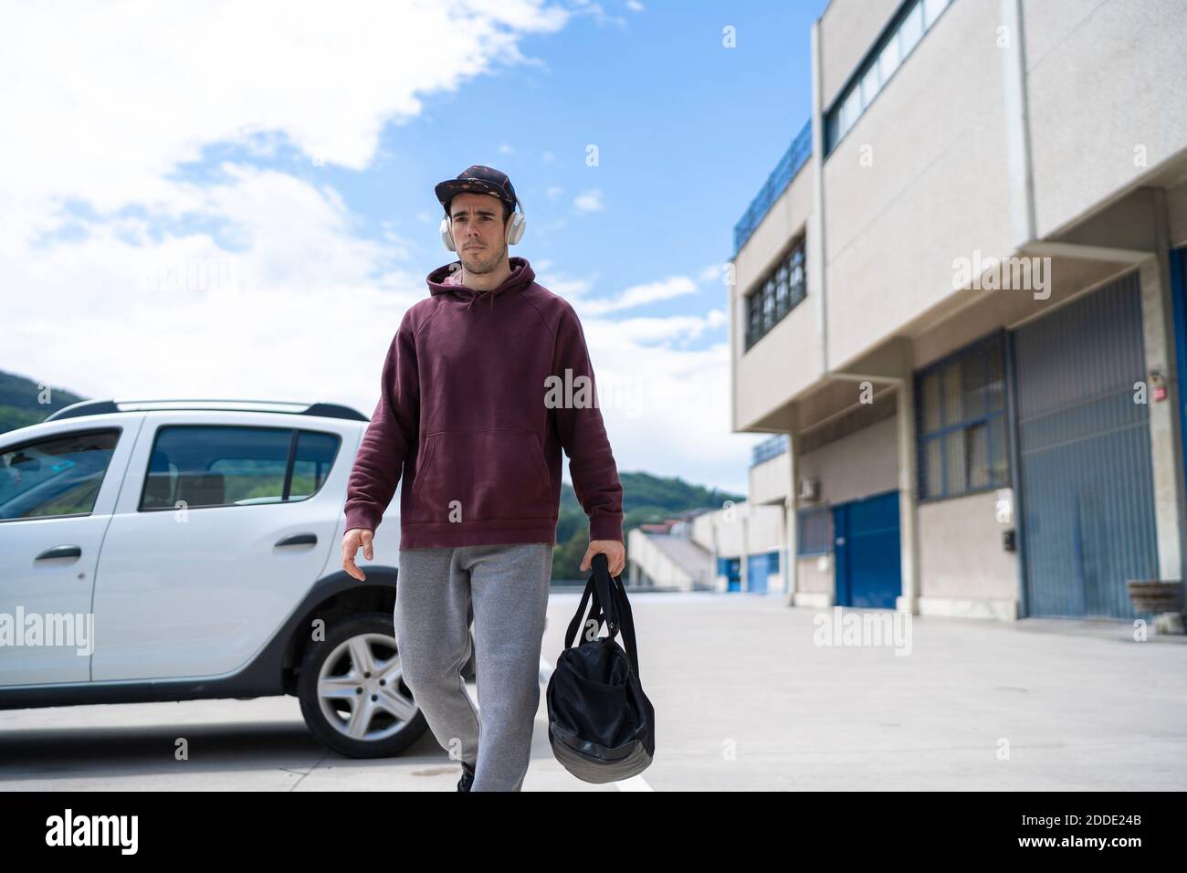 Uomo medio che cammina con borsa da palestra nel parcheggio il giorno di sole Foto Stock