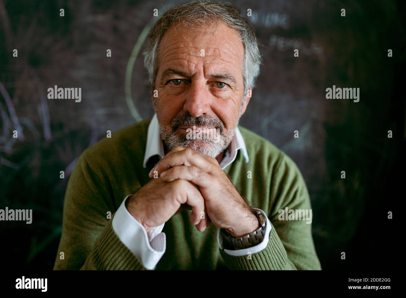 Uomo maturo con la mano sul mento seduto contro la lavagna a. casa Foto Stock