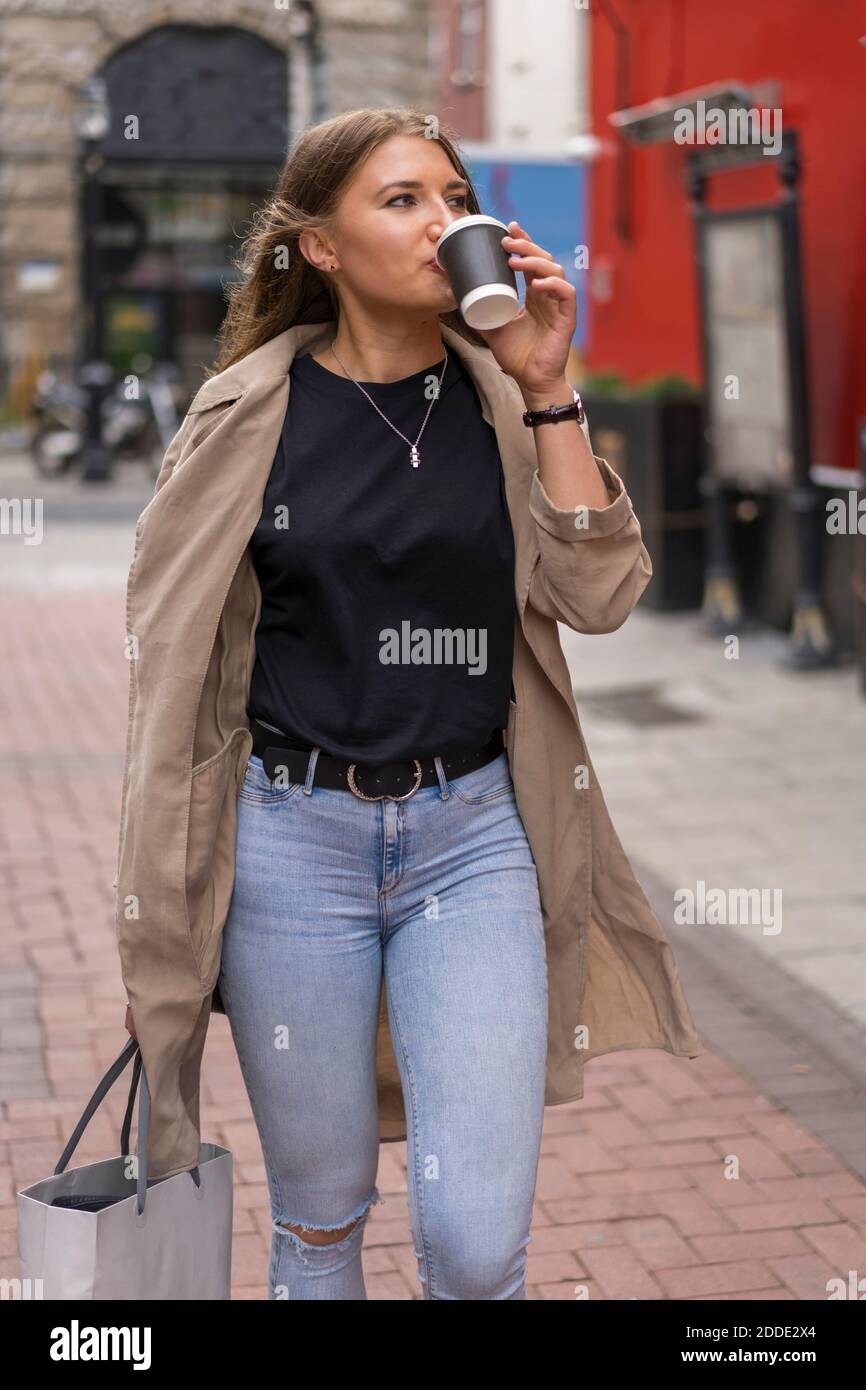 Giovane donna che beve caffè mentre si guarda via a piedi sulla strada Foto Stock