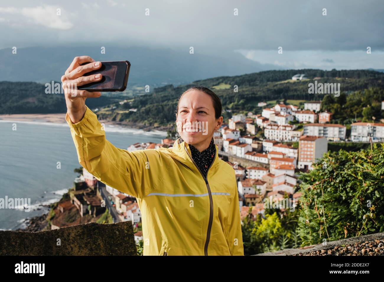 Donna sorridente che prende selfie con villaggio attraverso il telefono cellulare durante vacanze Foto Stock