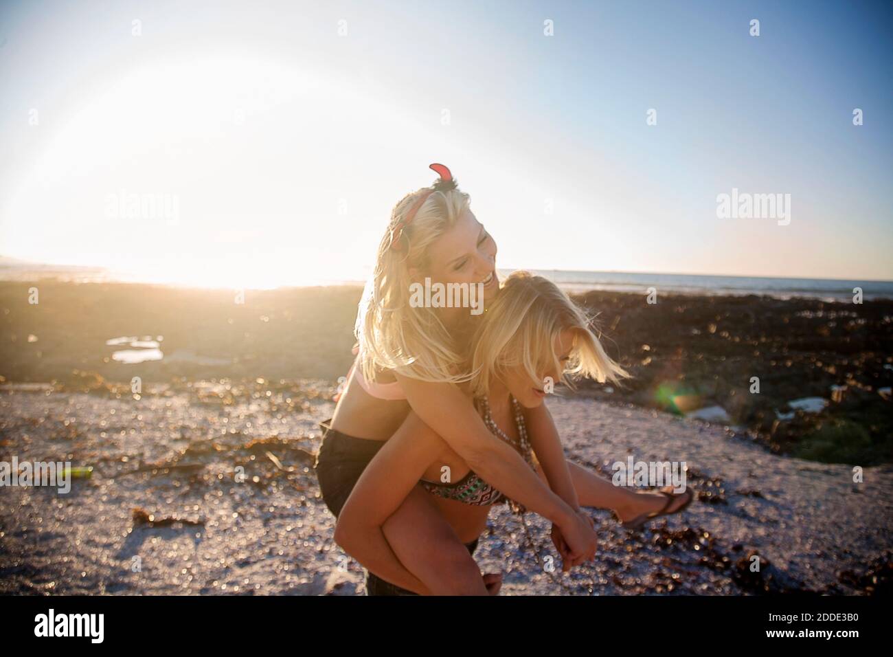 Giovane donna piggybacking allegra ragazza amica in spiaggia durante il tramonto Foto Stock