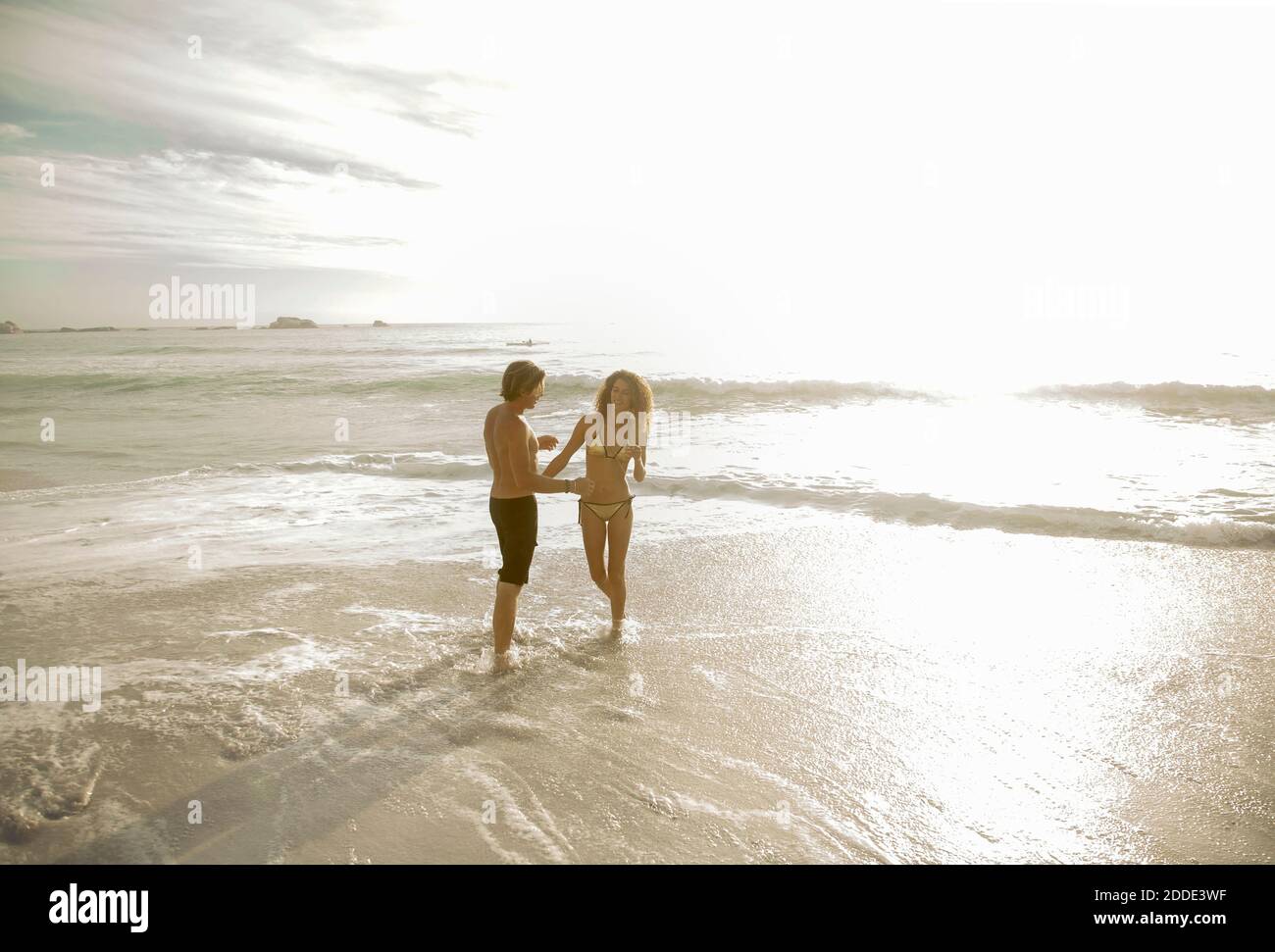 Coppia in piedi in acqua in spiaggia in giornata di sole Foto Stock