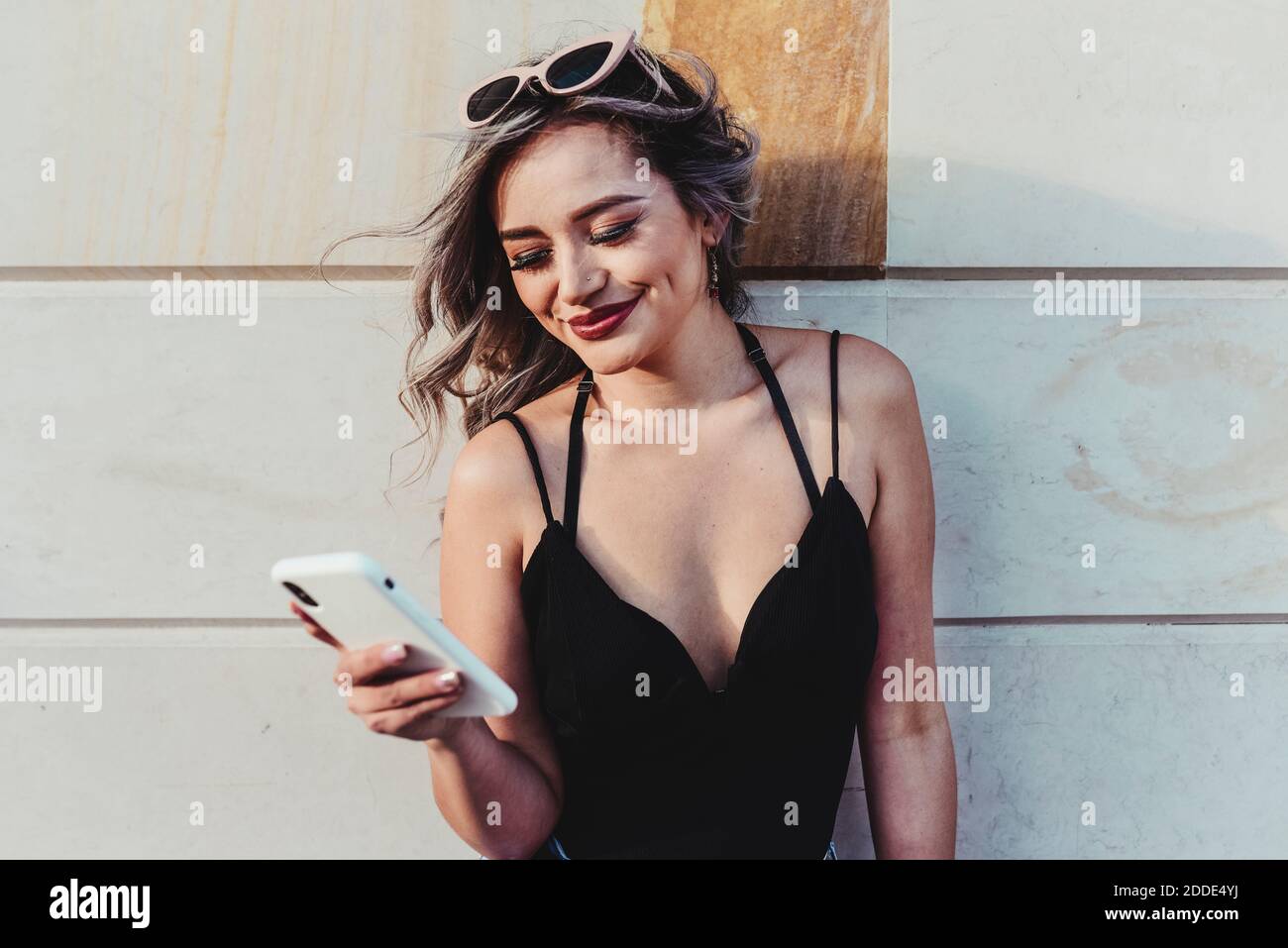 Messaggi di testo di una giovane donna sullo smartphone mentre si è in piedi parete Foto Stock