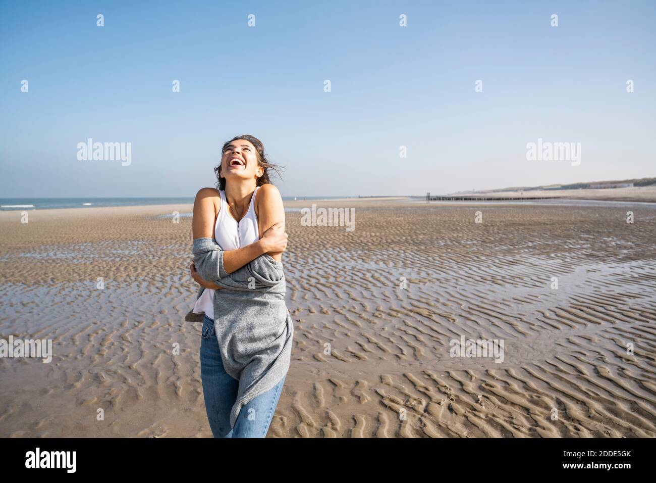 Felice giovane donna che si agguantano mentre in piedi alla spiaggia contro cielo limpido Foto Stock