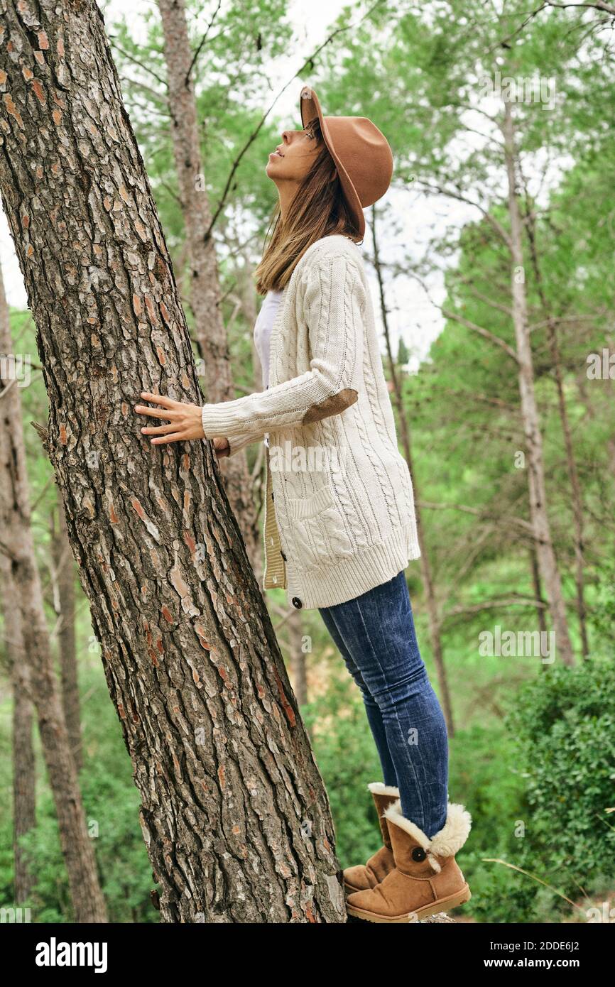 Donna che si tocca mentre si guarda su tronco di albero in foresta Foto Stock