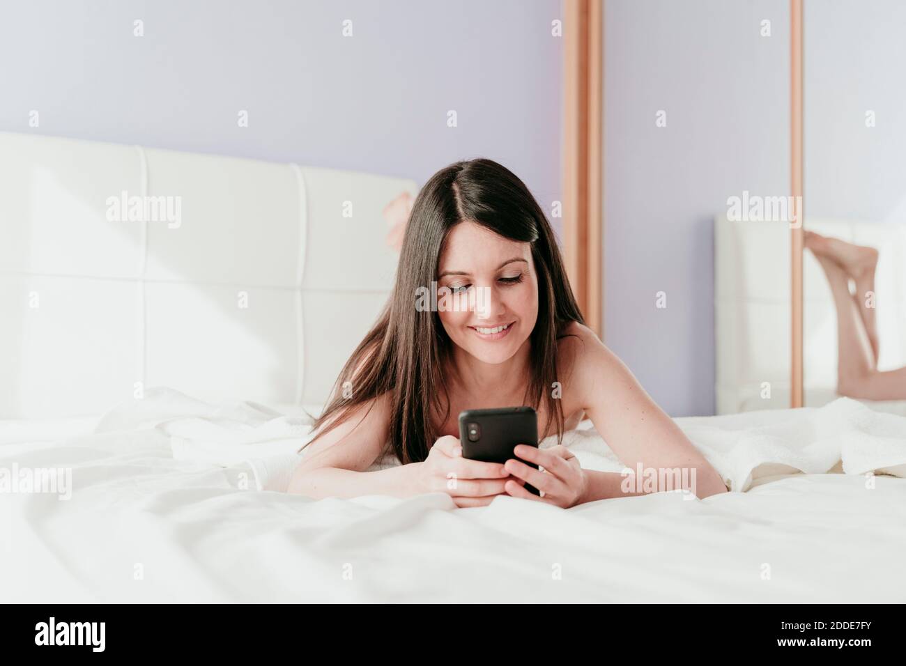 Sorridente bella donna di messaggi di testo mentre si sdraiava a letto a. casa Foto Stock