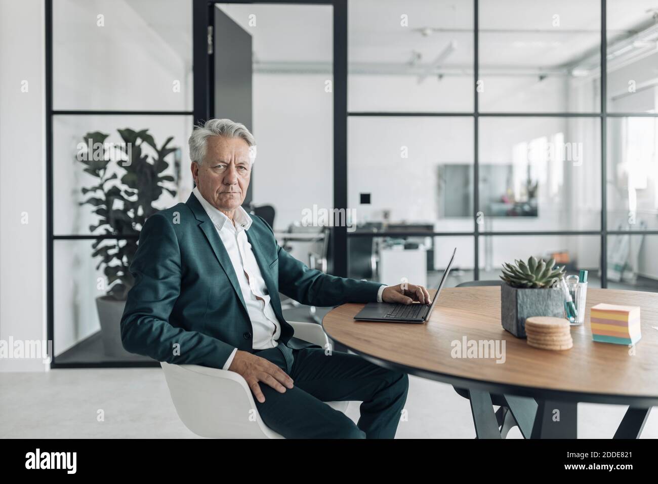 Uomo anziano che indossa il costume utilizzando il computer portatile mentre si siede sulla sedia in ufficio Foto Stock
