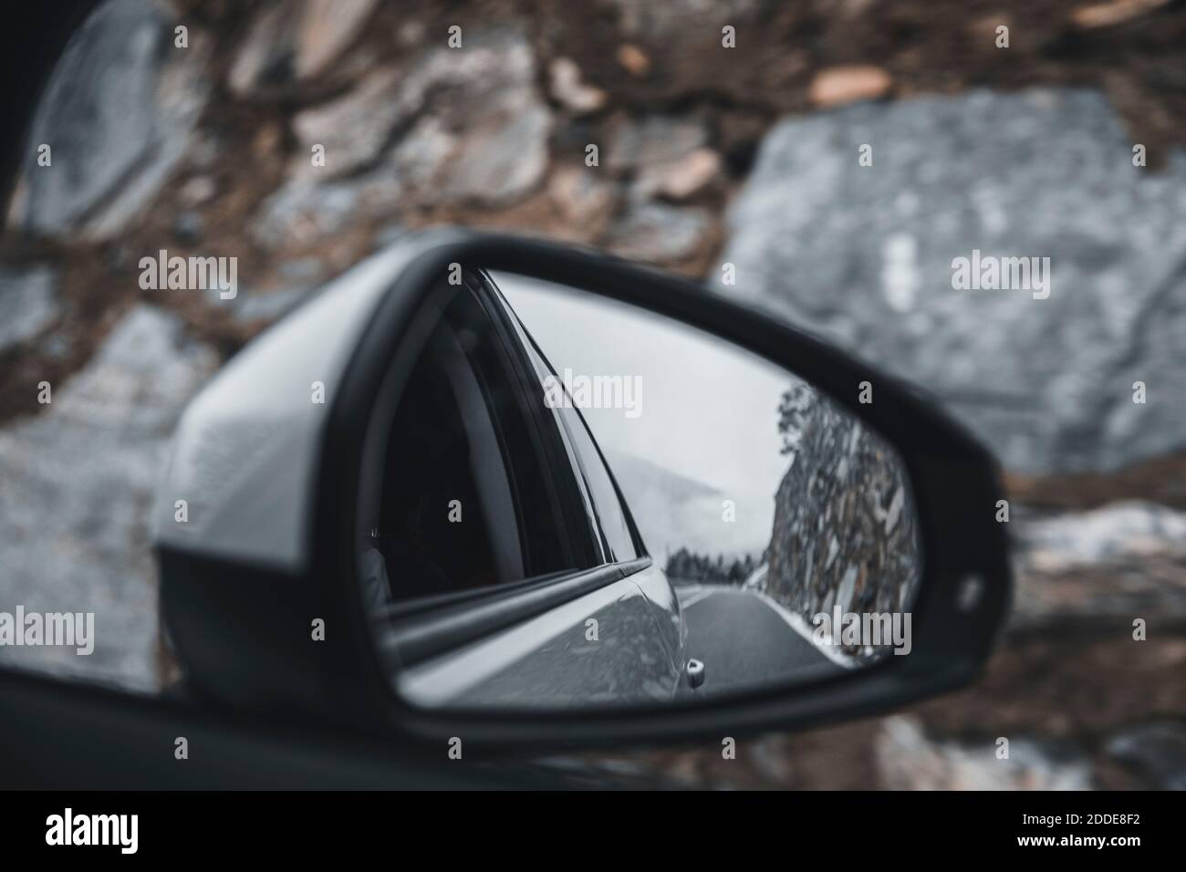 Specchio retrovisore laterale che riflette la guida di un'auto lungo le autostrade alpine Foto Stock