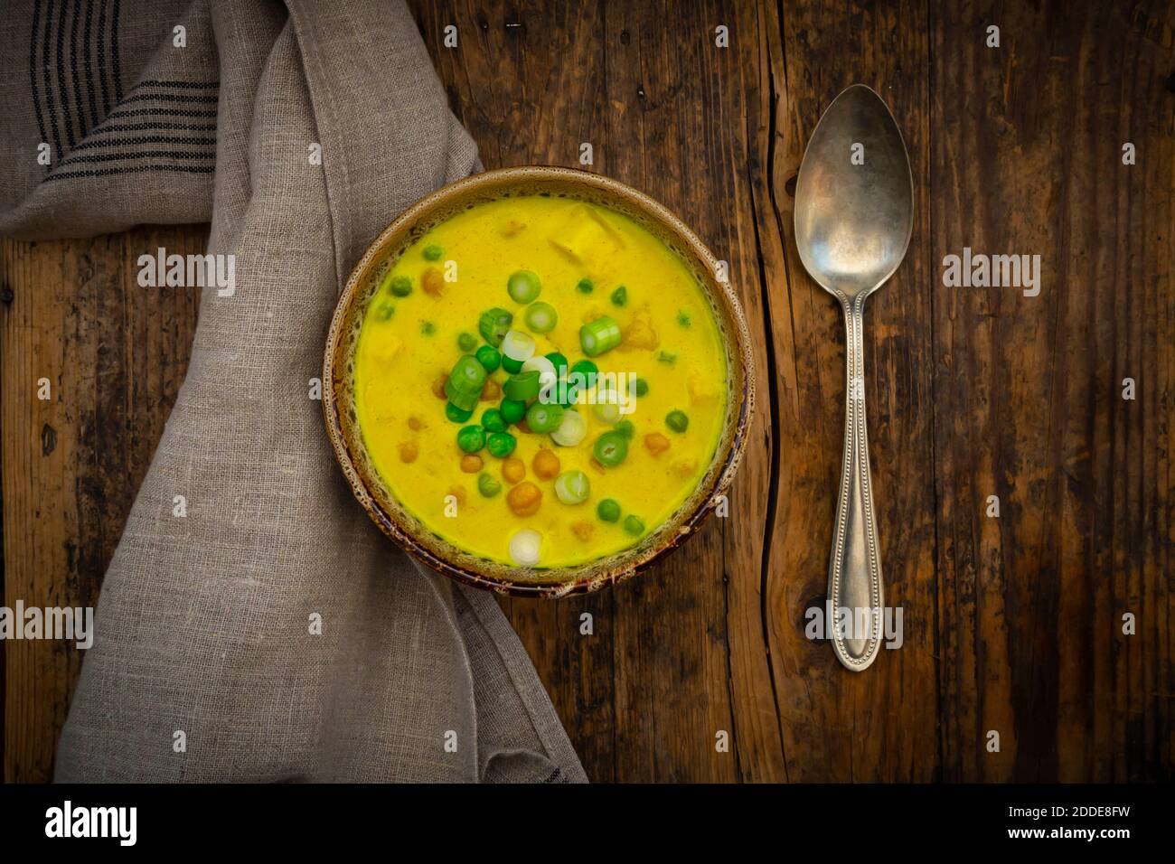 Ciotola di zuppa di cocco vegana con piselli verdi, ceci, scalogno e curcuma Foto Stock