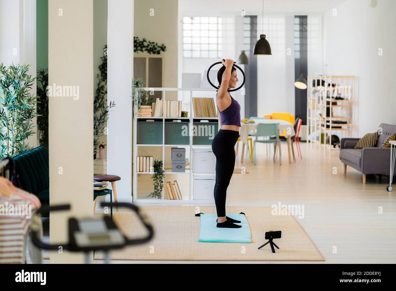 Influencer femminile che si esercita con pilates ring e video registrazione su fotocamera a casa Foto Stock