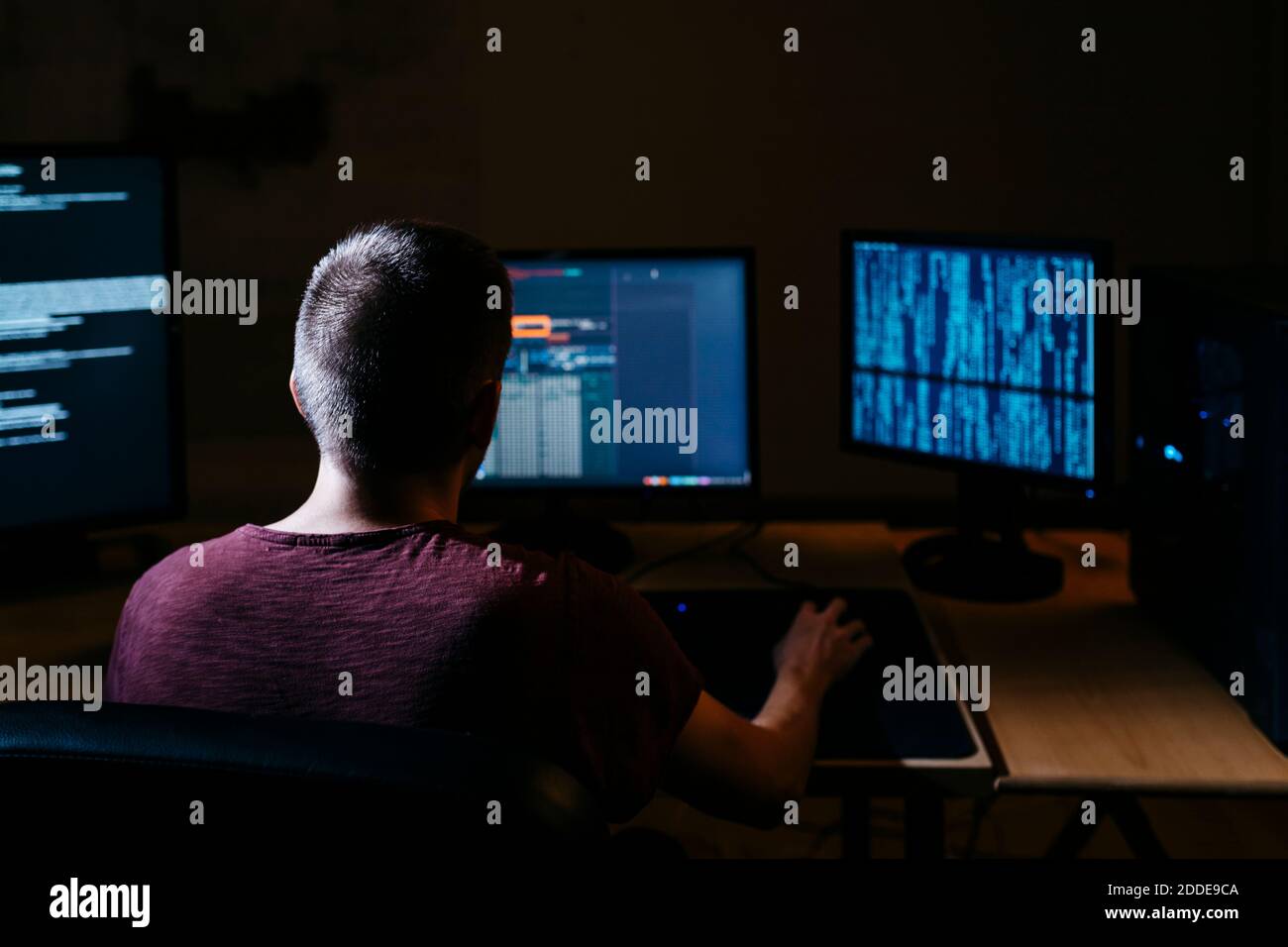 Hacker che utilizza il computer mentre si è seduti in un ufficio buio Foto Stock
