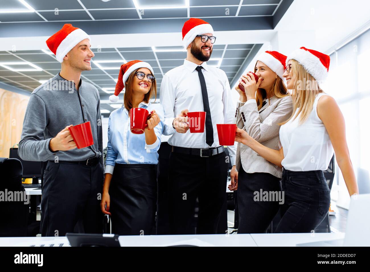 Felici i giovani uomini d'affari nei cappelli di Babbo Natale che celebrano una vacanza in un ufficio moderno. Gruppo di giovani uomini d'affari che bevono un drink e si divertono Foto Stock