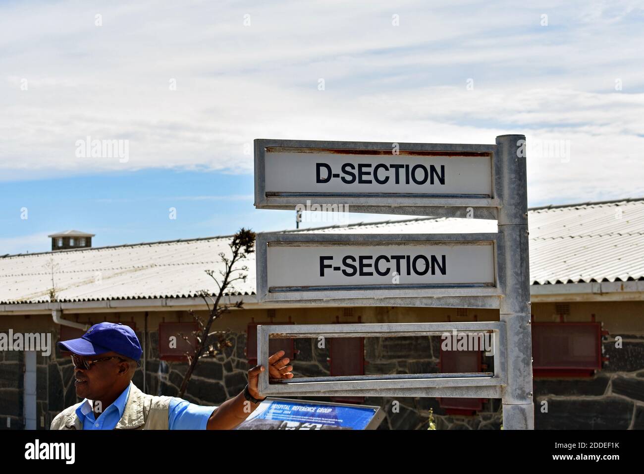 Una guida turistica si appoggia su un cartello che indica la strada per la sezione D e F, diverse ali nella prigione di massima sicurezza sull'isola di Robben, Città del Capo. Foto Stock