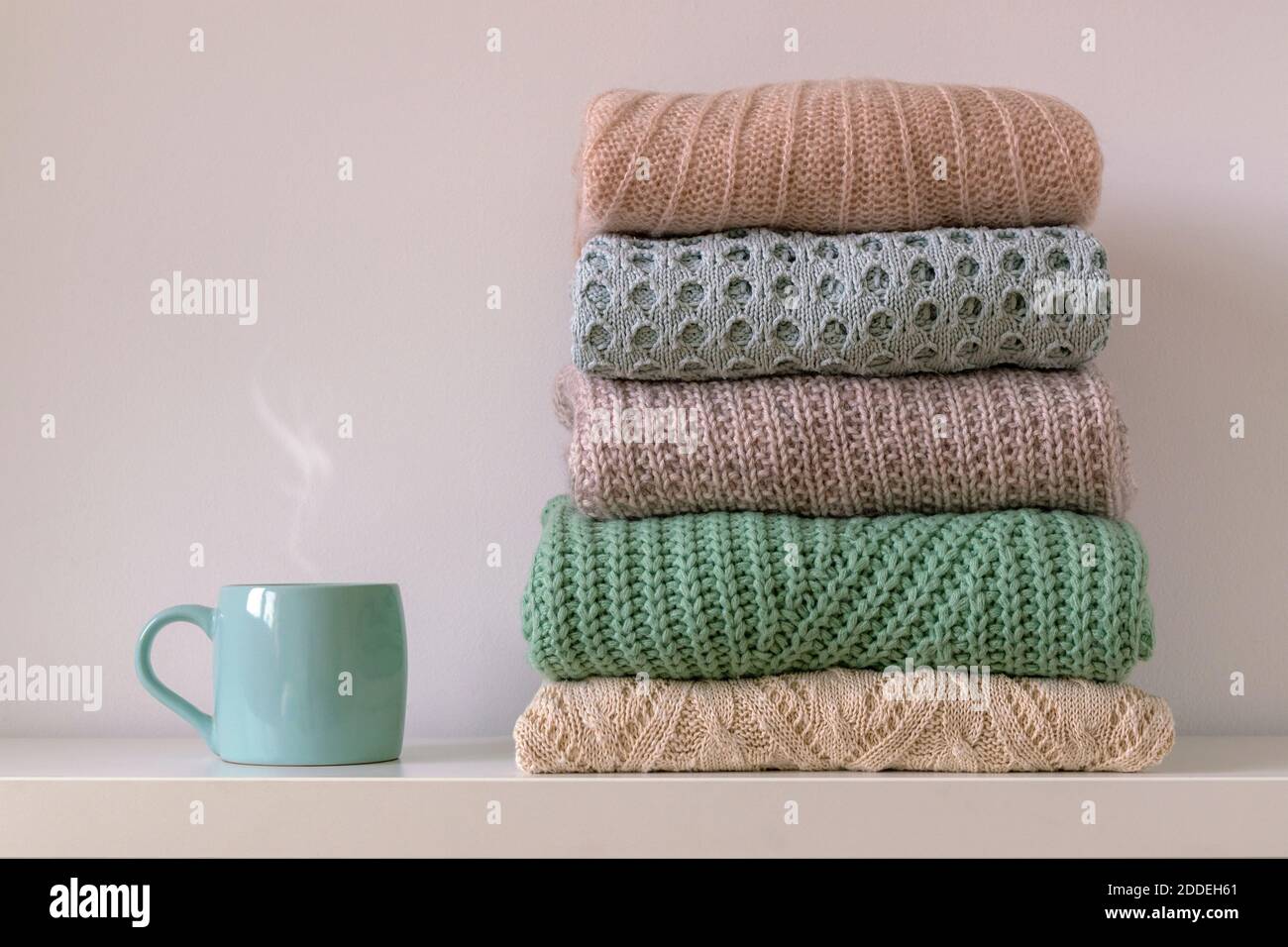 Pila di caldo e accogliente maglia da donna pullover e tazza di bevanda calda su sfondo bianco. Concetto di comfort in autunno o inverno. Foto Stock