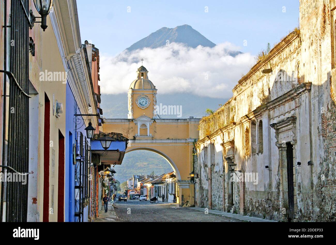 Il vulcano Agua, protetto dalle nuvole, è uno dei tre vulcani che si affacciano sulla città coloniale di Antigua, Guatemala. Vista da Calle del Arco, la Via dell'Arco, il monumento vulcanico offre uno sfondo per l'Arco di Santa Catalina, un monumento storico costruito nel 1694. L'arco, storicamente, ha collegato due conventi, Convento della Vergine e Convento di Santa Catalina. Le monache erano tenute a non essere viste in pubblico così l'arco ha una passerella segreta affinchè loro attraversi fra i due conventi. L'orologio all'aperto in stile francese sull'arco è stato aggiunto nel 1800 e deve essere avvolto ogni tre giorni. Foto Stock