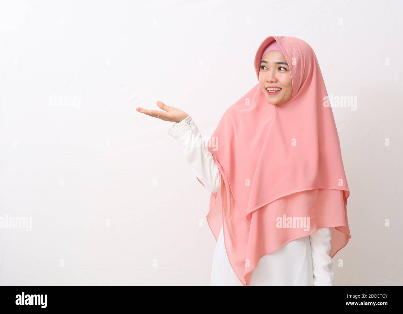 Un ritratto della donna musulmana asiatica felice che indossa un velo o un hijab poiting o che presenta qualcosa accanto a lei. Isolato su sfondo bianco con copia spac Foto Stock