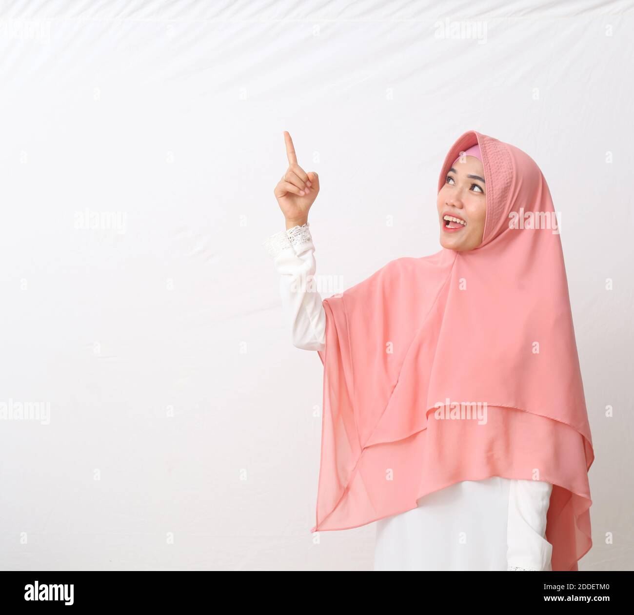Un ritratto della donna musulmana asiatica felice che indossa un velo o un hijab sorridente e guardando lo spazio vuoto mentre indica qualcosa. Isolato su sfondo bianco Foto Stock