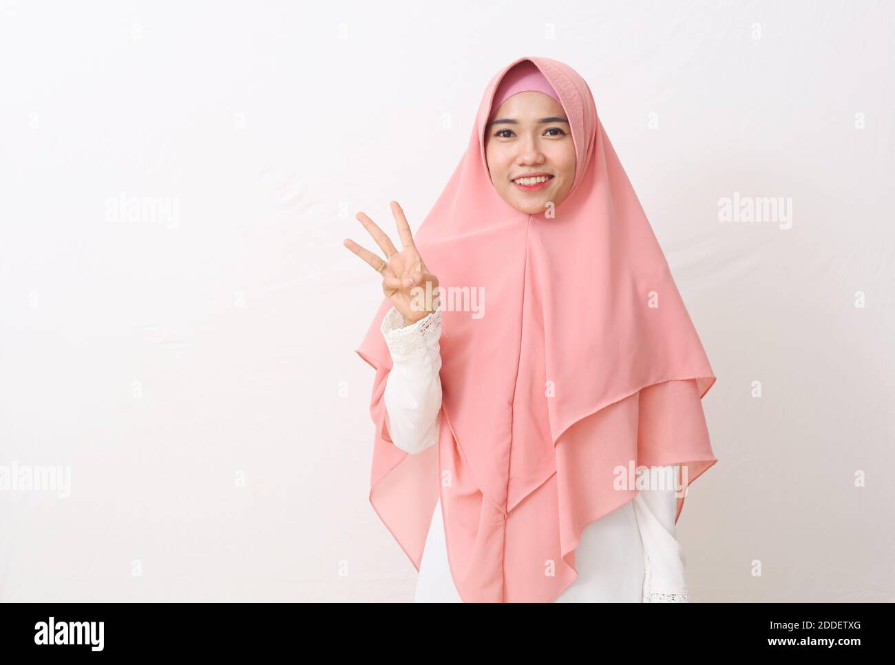 Un ritratto della donna musulmana asiatica felice che indossa un velo o un hijab mostrando e puntando in su con le dita numero tre mentre sorride fiducioso. Isolato su Foto Stock