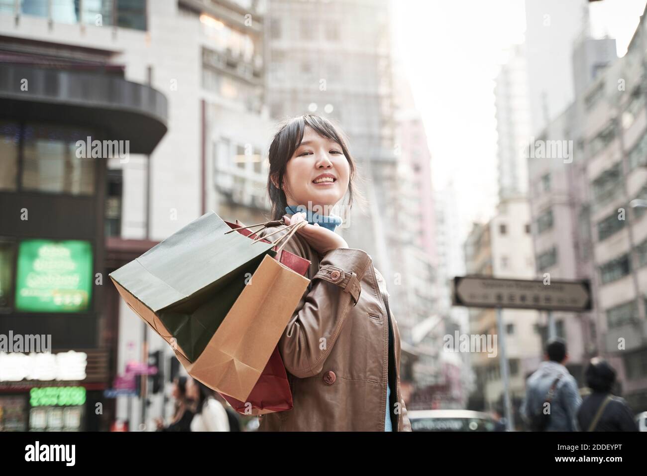 felice giovane donna asiatica che porta borse per lo shopping a piedi in città via Foto Stock