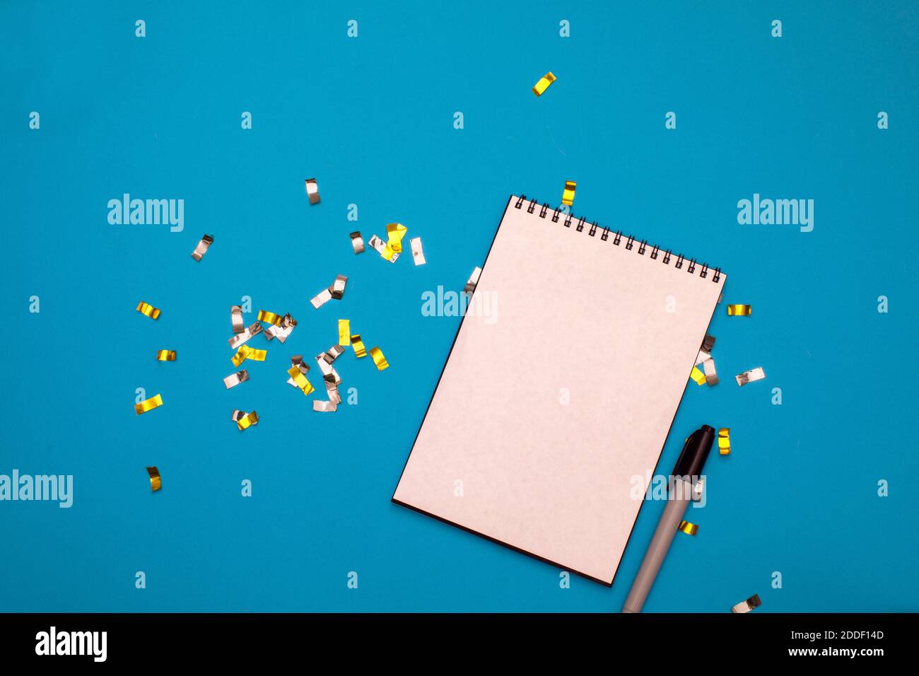 Il blocco note wishlist con un marcatore giace su uno sfondo blu con confetti dorati Foto Stock