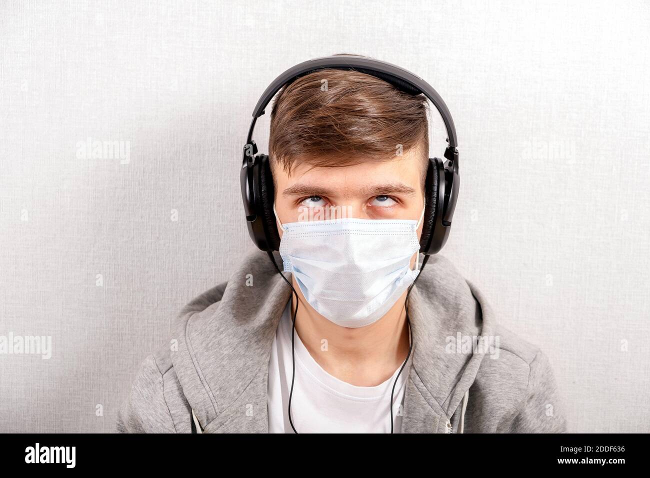 Irritato giovane uomo in cuffie e maschera influenza da Parete nella stanza Foto Stock