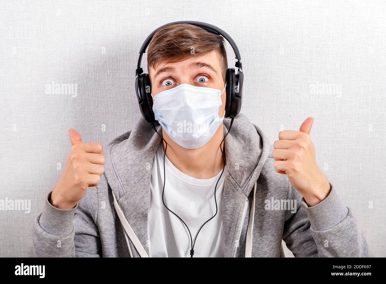 Happy Young Man in cuffie e influenza Mask ascoltare La musica e spettacolo OK Gesture Foto Stock