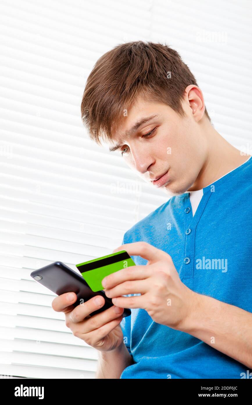 Ragazzo tormentato con un telefono e una carta di banca Sullo sfondo di Jalousie Foto Stock