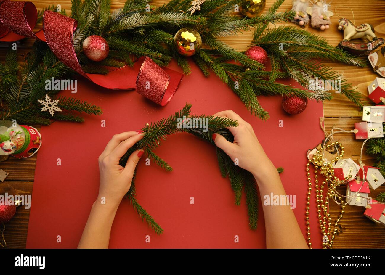 Mani che fanno la corona di Natale rustica s su uno sfondo rosso. Immagine della moodia atmosferica al workshop di vacanza Foto Stock