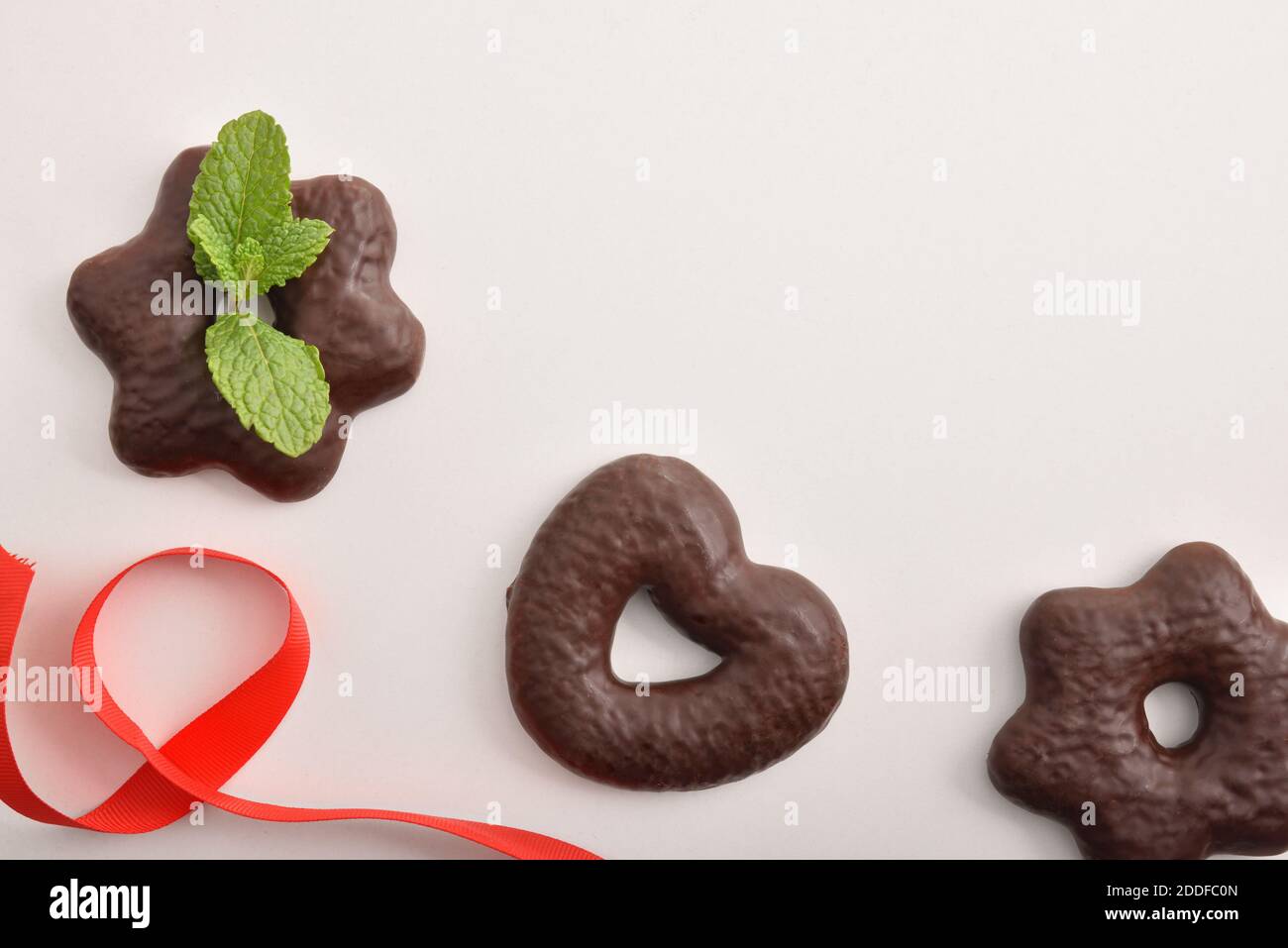 Biscotti romantici immersi in cioccolatini a forma di stella e cuore su tavola bianca con arco rosso. Vista dall'alto. Composizione orizzontale. Foto Stock