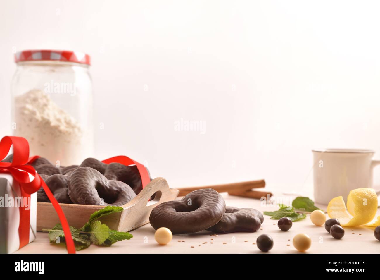 Biscotti di cioccolato a forma di cuore e stella su vassoio e menta, bastoncini di cannella e limone su tavolo di legno con regali e tazza di infusione sfondo isolato. Fro Foto Stock