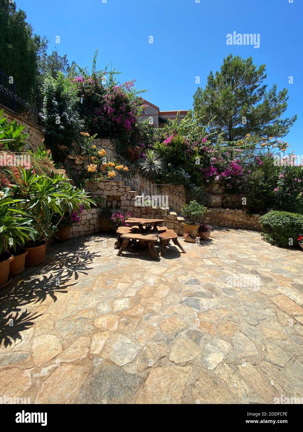 Giardino floreale segreto di villa privata di vacanza estiva. Piante e fiori colorati con una scrivania in legno nella terrazza della casa estiva. Foto Stock
