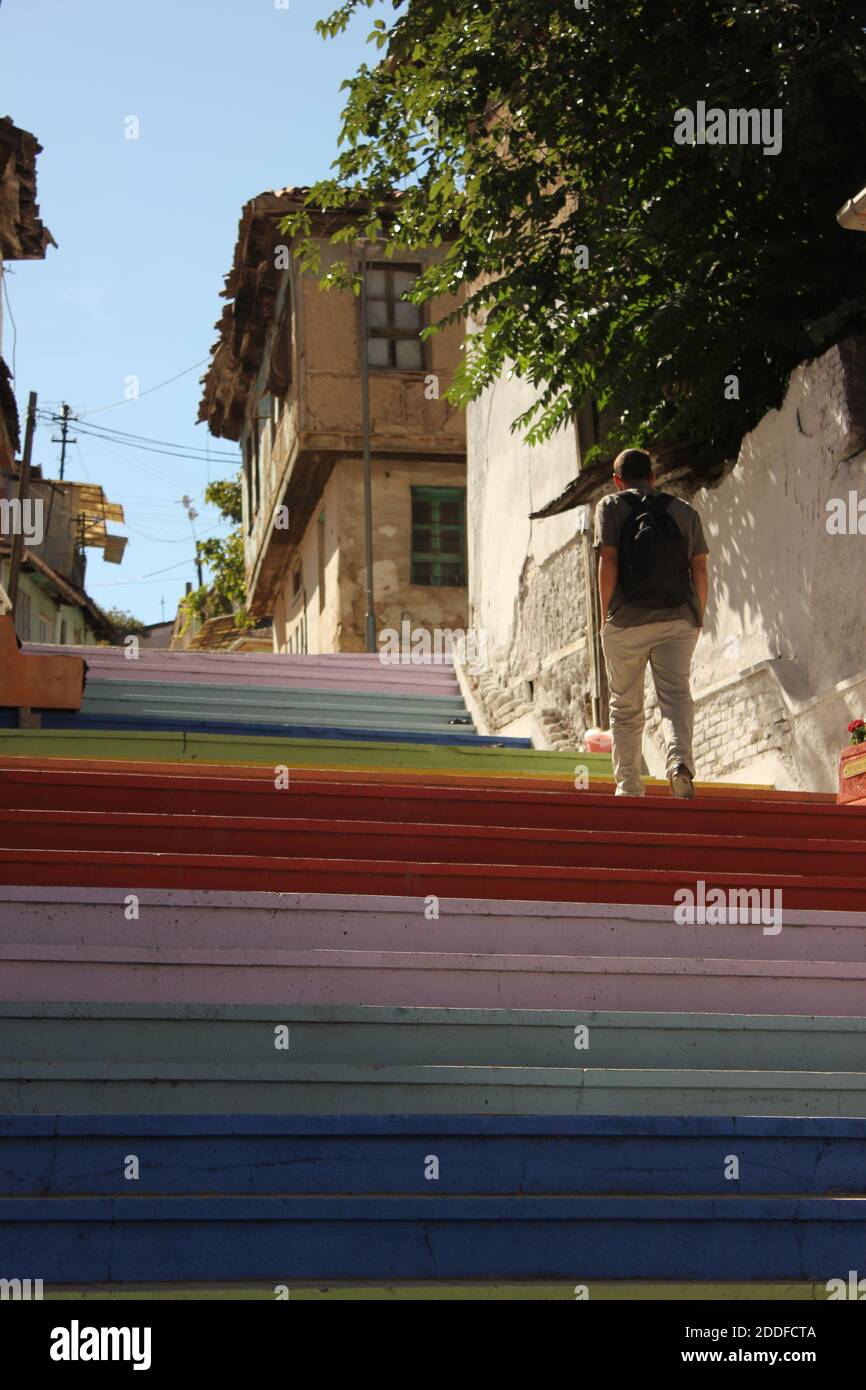 Uomo con zainetto che sale scale colorate dipinte. Via delle scale dipinte dai colori arcobaleno. Vecchia casa e muro. Foto Stock