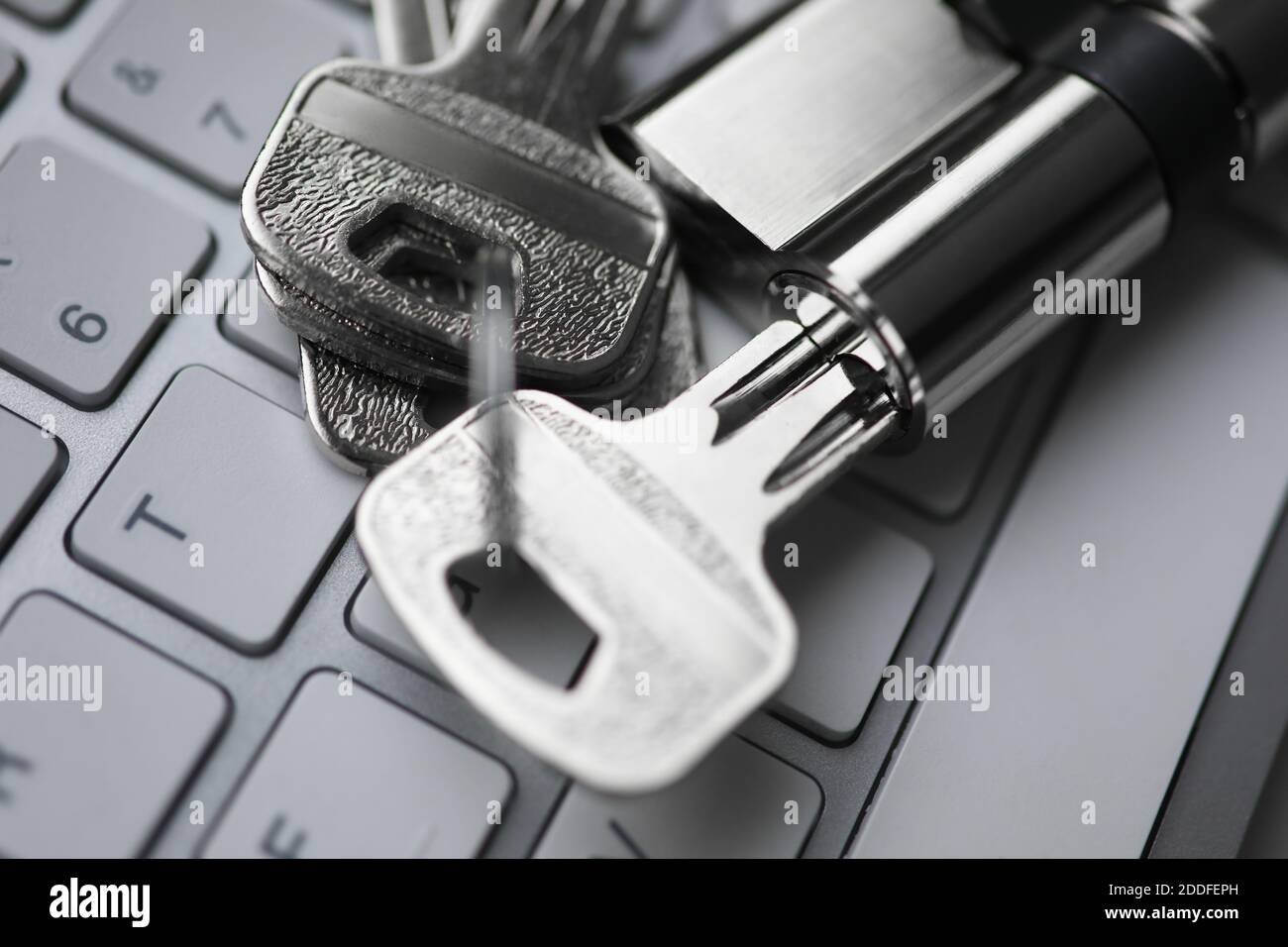 Chiave argentata con lucchetto giace sul retro del closeup della tastiera bianca. Foto Stock