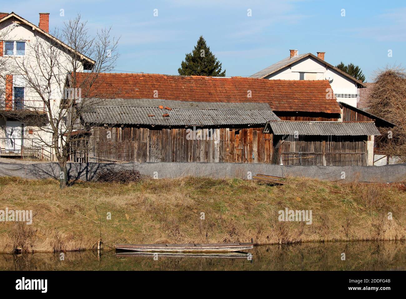 Vecchio fienile di legno allungato con area di deposito e mais di legno capannone costruito accanto al tranquillo fiume protetto da alluvioni parete composta da barriere scatolate Foto Stock