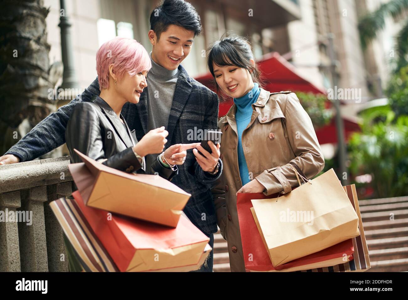 tre giovani asiatici alla moda persone che navigano utilizzando il cellulare durante lo shopping in città Foto Stock