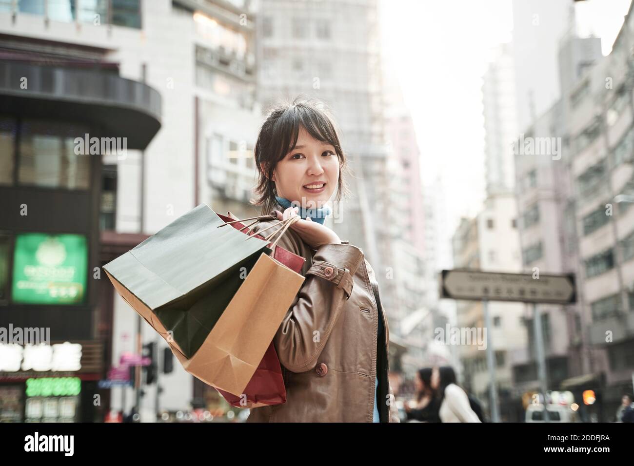 felice giovane donna asiatica che porta borse per lo shopping a piedi in città via Foto Stock