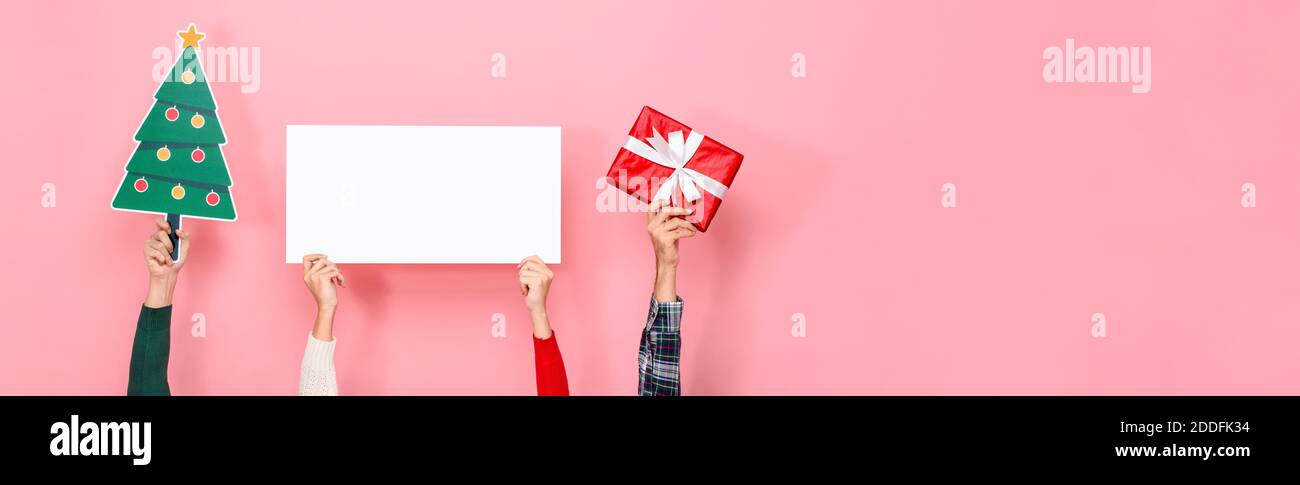 Mani che tengono scatola regalo, albero di Natale e lavagna di carta bianca con spazio vuoto per il testo in sfondo rosa isolato banner Foto Stock