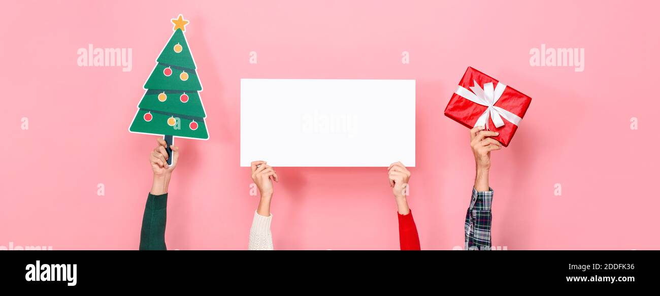 Mani che tengono scatola regalo, albero di Natale e lavagna di carta bianca con spazio vuoto per il testo in sfondo rosa isolato banner Foto Stock