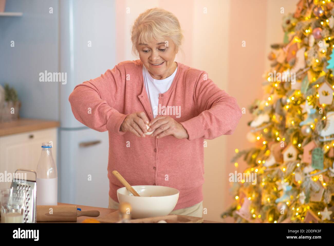 Donna sorridente dai capelli grigi che rompe le uova nella ciotola Foto Stock