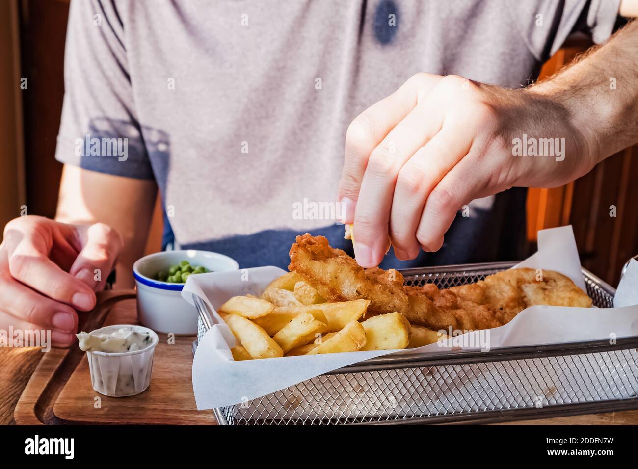 Spruzzare a mano dell'uomo con pesce limone e patatine Foto Stock