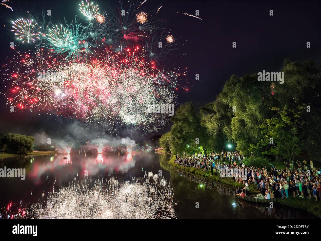 Folla di persone che guardano fuochi d'artificio e il loro riflesso in un fiume o lago, molte persone che scattano foto con il loro telefono Foto Stock