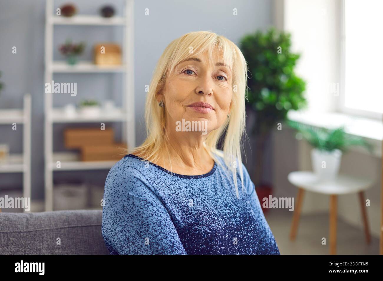 Ritratto di una donna matura che sorride guardando la fotocamera mentre si siede su un divano. Foto Stock