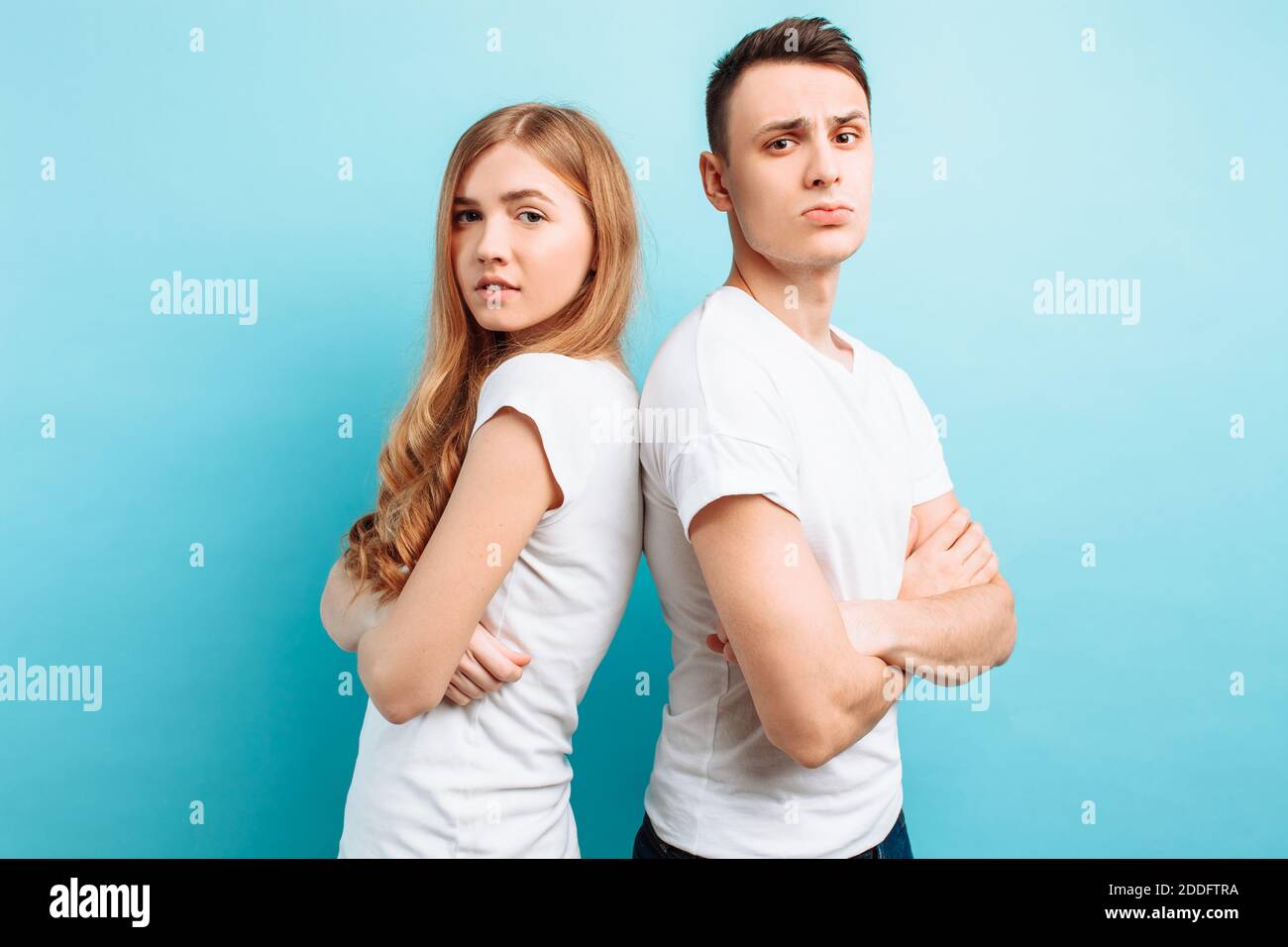 Felice coppia amorosa, uomo e donna, vestita con T-shirt bianche, ritorno a schiena e sorridente, su sfondo blu Foto Stock