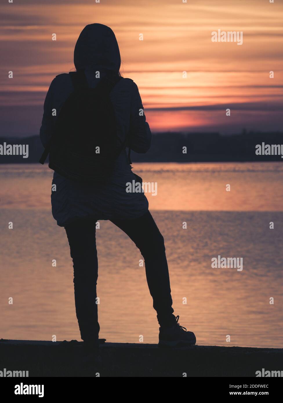 Ragazza che ammira il bellissimo tramonto ai margini di un lago. Foto Stock
