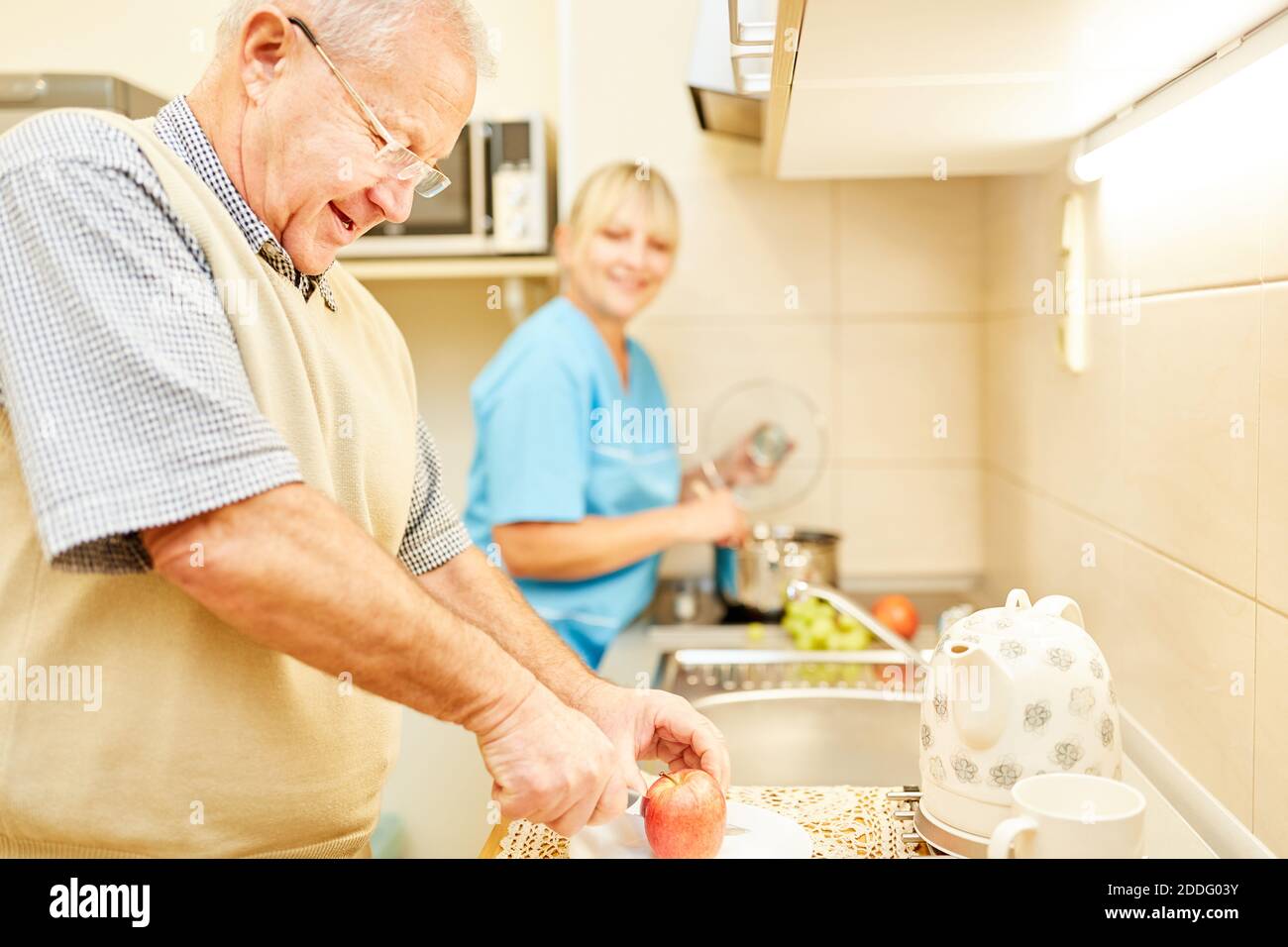 Senior taglia una mela in cucina di un senior sorvegliato appartamento cittadino con caregiver Foto Stock