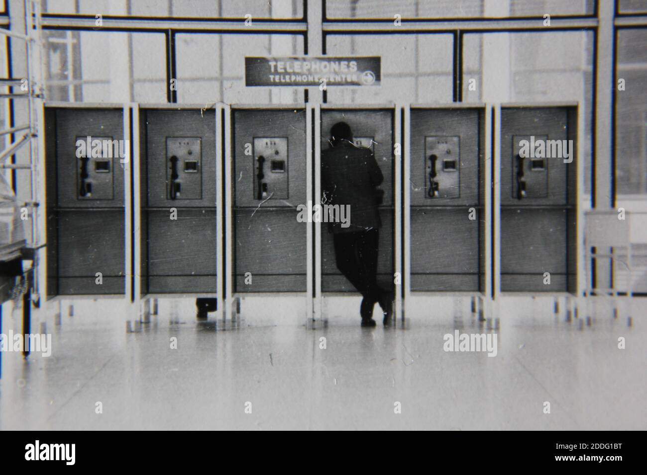 Bella fotografia in bianco e nero degli anni '70 di un normale ragazzo che parla su un telefono fisso pubblico in una lobby pubblica. Foto Stock