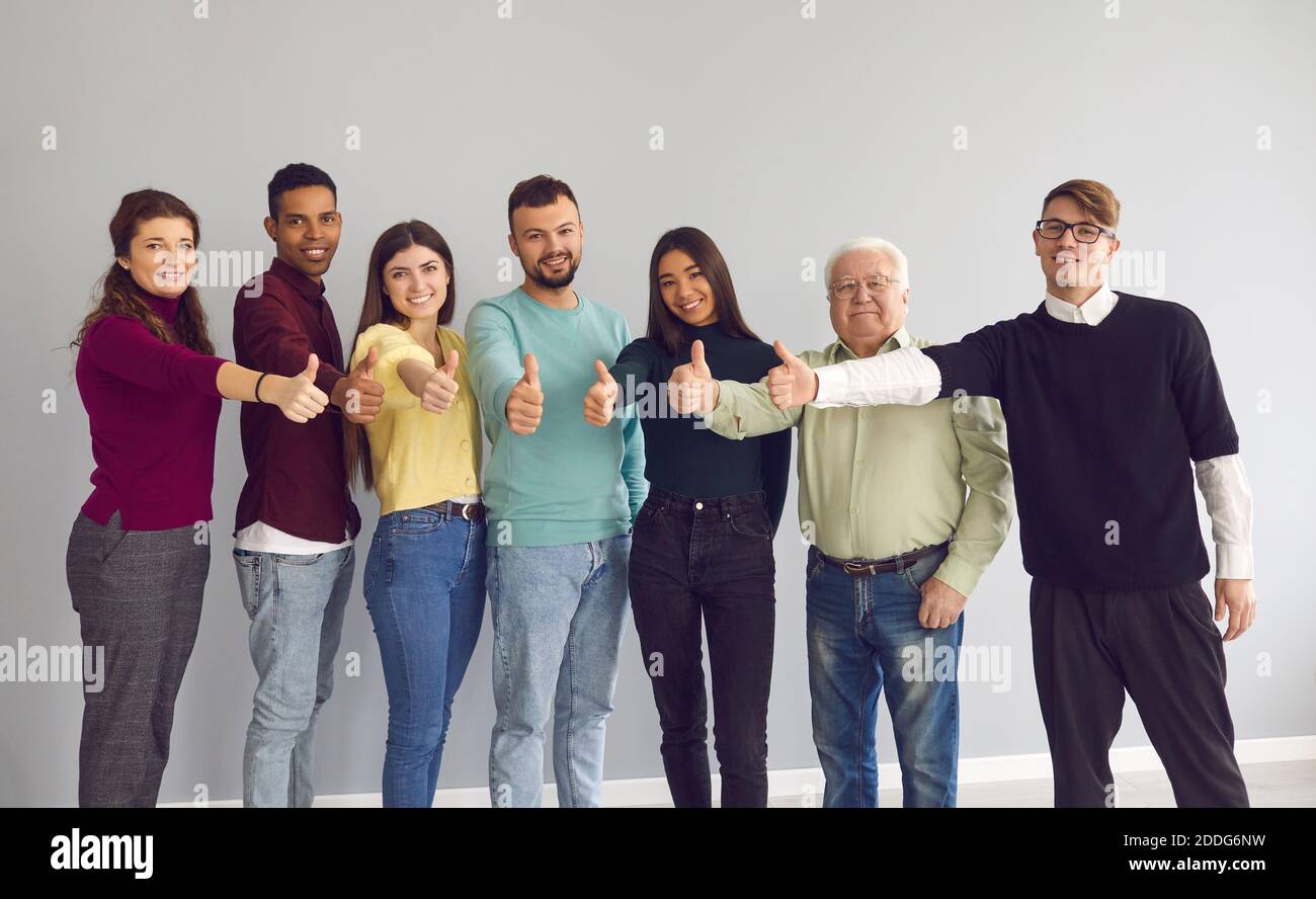 Gruppo di persone felici e diverse che si levano in piedi insieme, dando i pollici e guardando la fotocamera Foto Stock