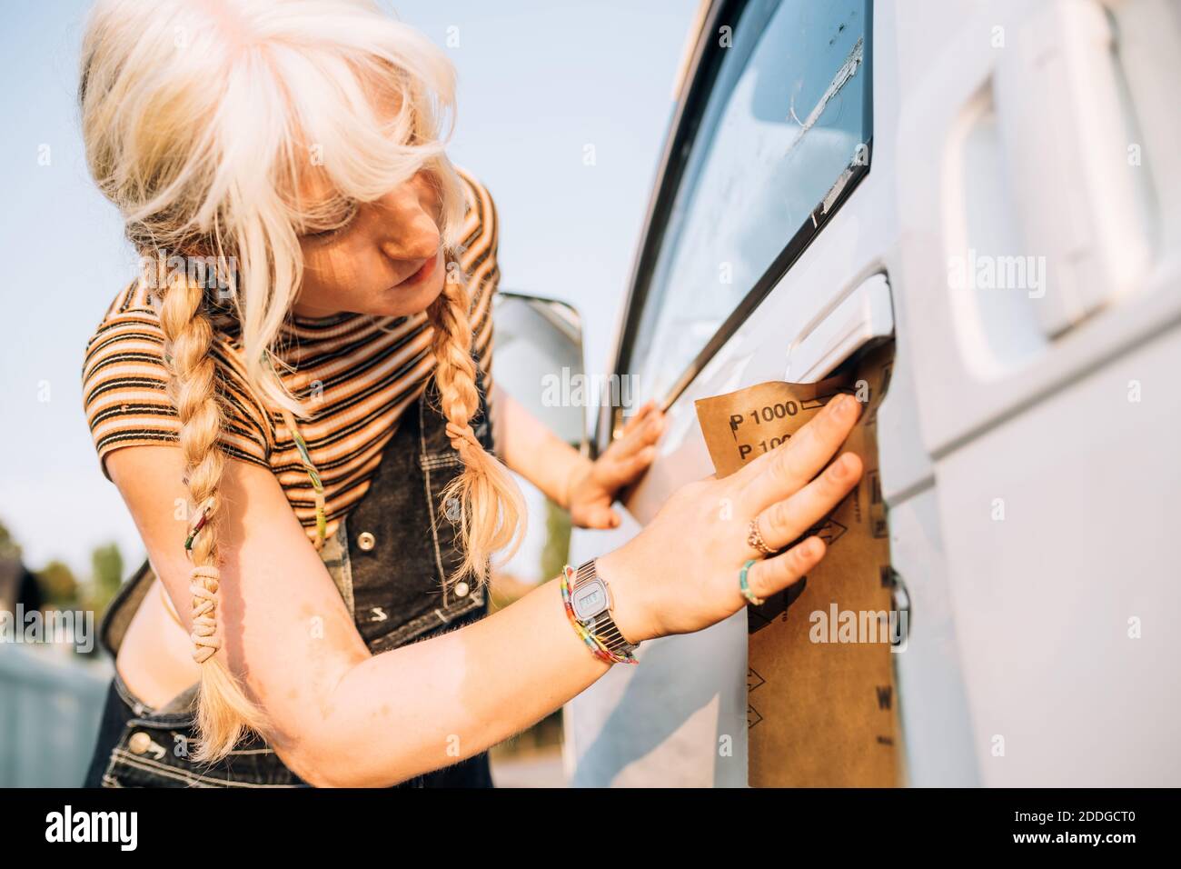 Giovane donna che usa carta vetrata sul suo furgone Foto Stock