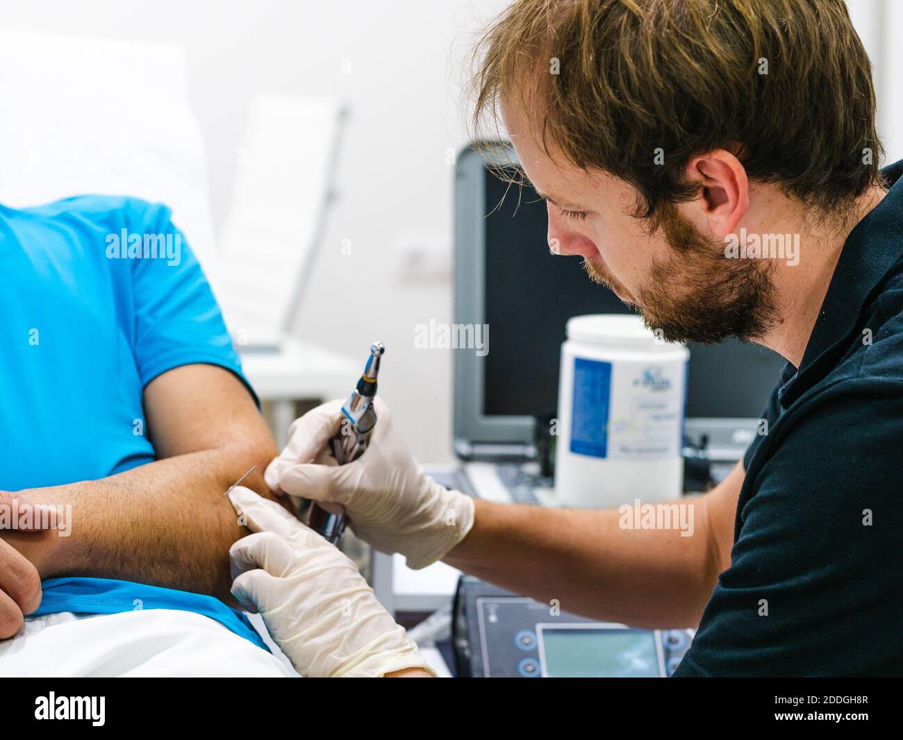 Vista laterale del medico maschile in occhiali di protezione utilizzando sonda laser per la cura del braccio del paziente durante il lavoro in clinica di fisioterapia Foto Stock